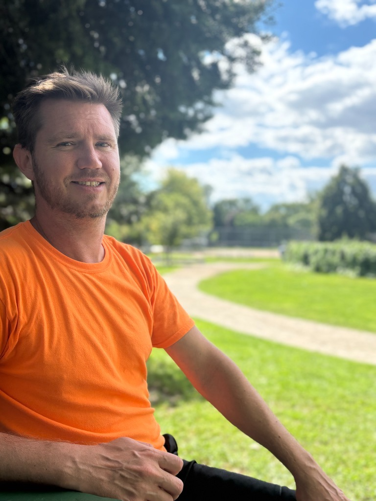 Mark Ucieklak, founder of Get Active 'N Play, smiling in an orange T-shirt in a park