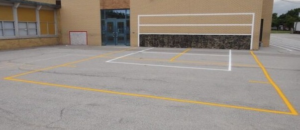 A volleyball net painted on a schoolyard wall with the court marked out on the pavement in front of it