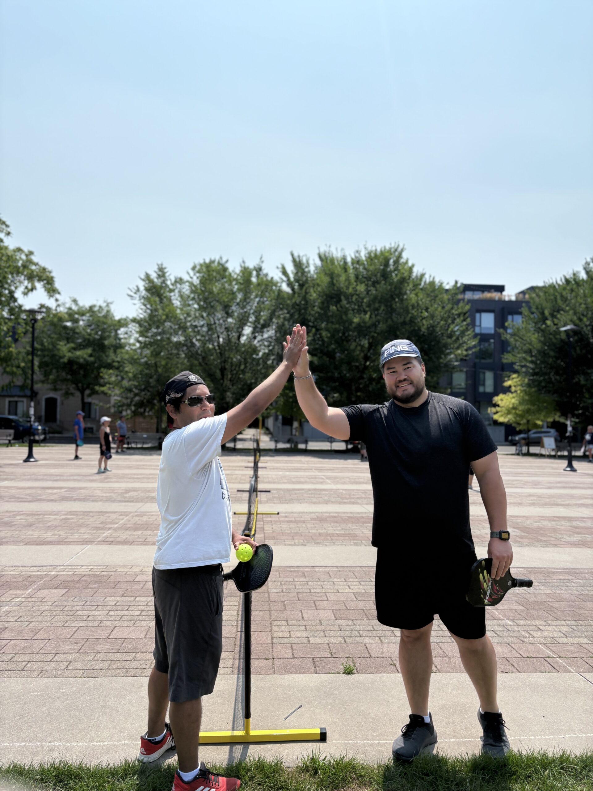 Two pickleball players high-five beside a portable net at Sorauren Park