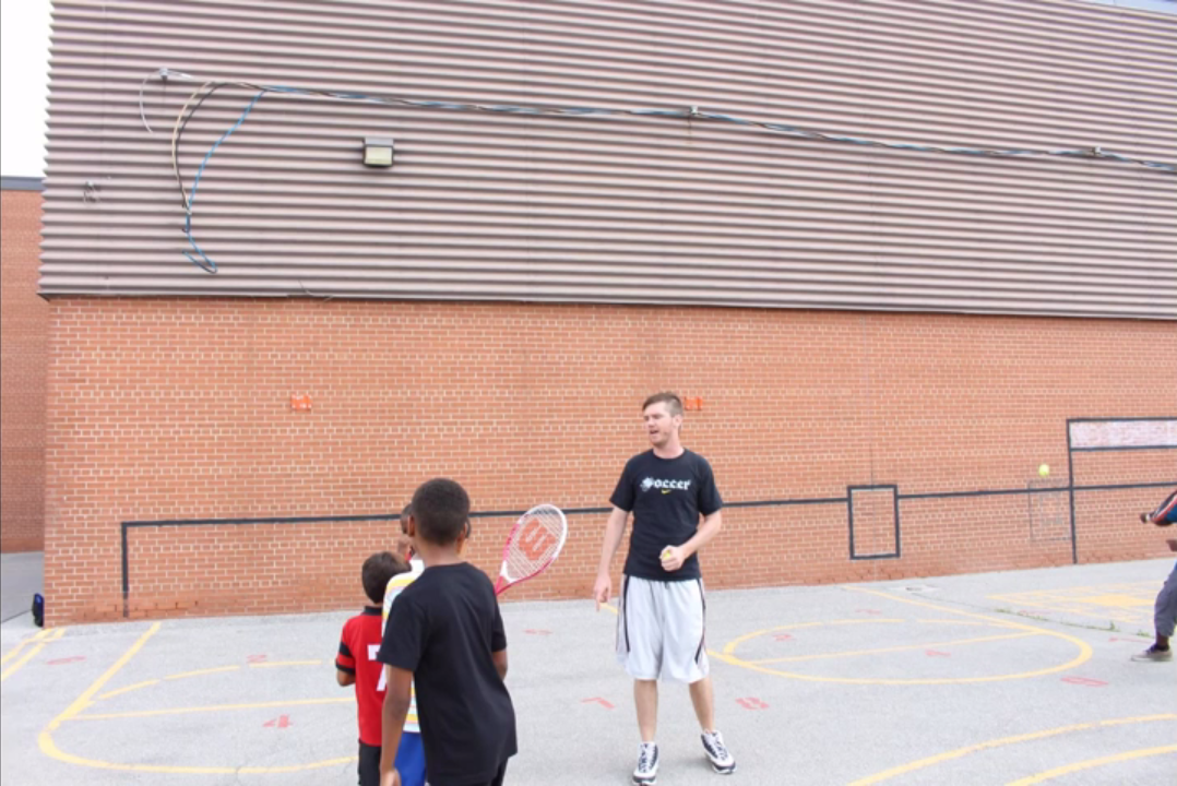 GANP founder Mark speaking with children beside an early schoolyard Sportswall