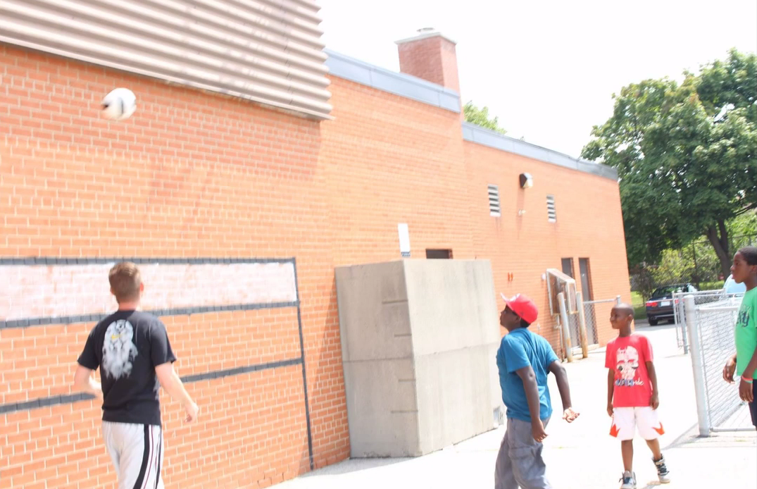 Children playing beside an early Sportswall during a schoolyard activity