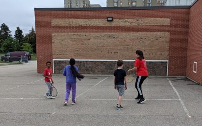 3 kids and an adult are having fun playing tennis using an elementary schools outdoor tennis sportswalls